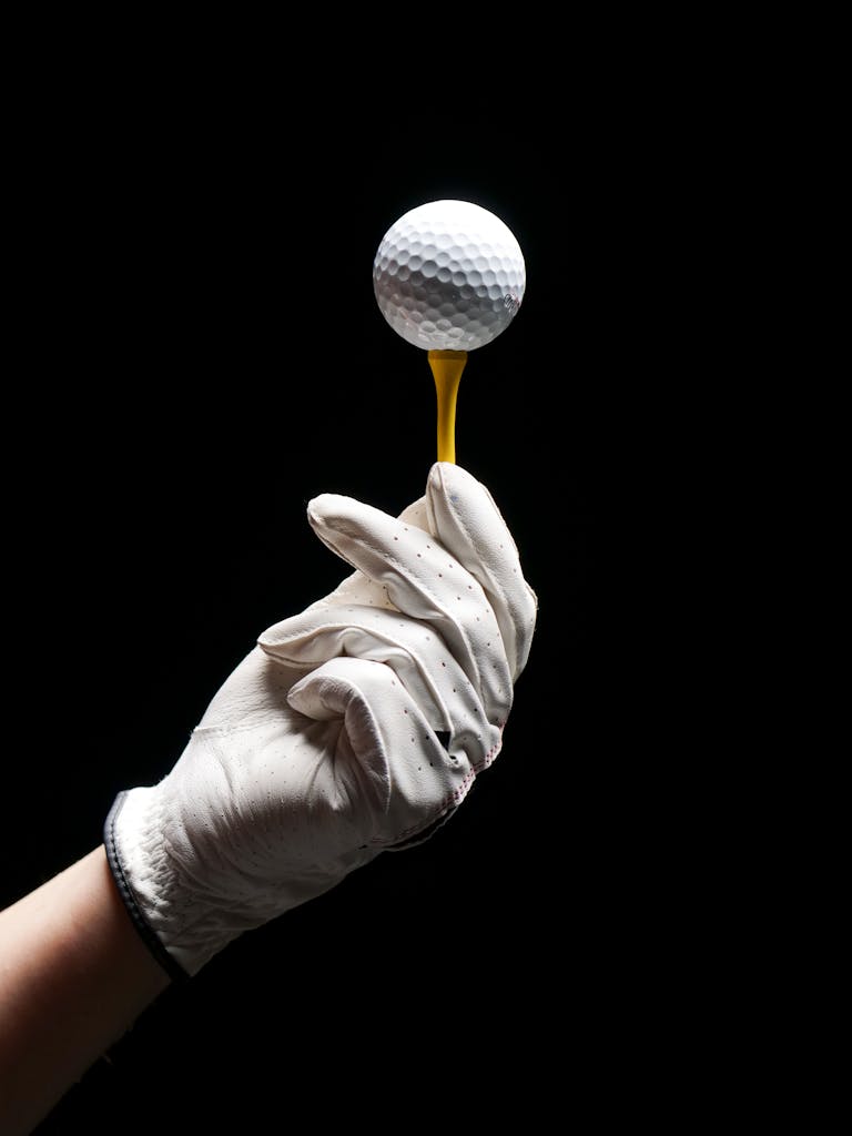 person wearing gloves holding golf tee with ball